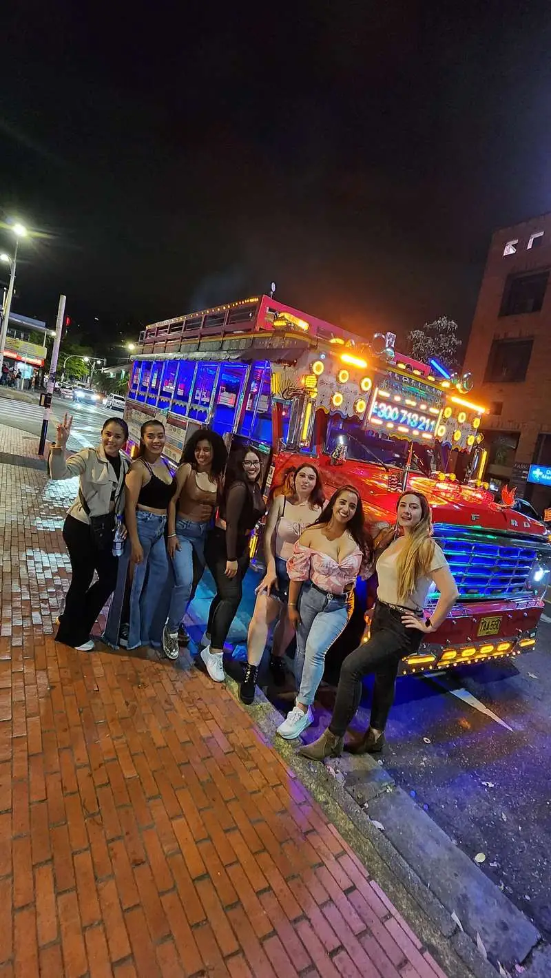Tourists dancing on a colourful Chiva party bus with DJ through the streets of Medellin Colombia nightlife district